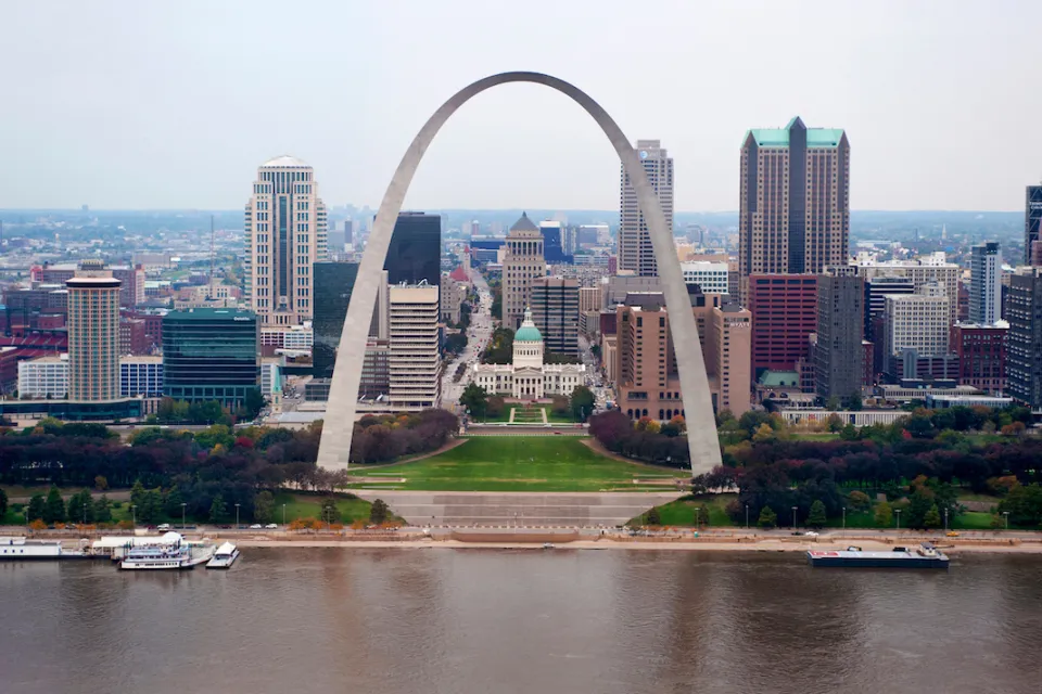 View of the Gateway Arch with Mississippi River in foreground and St. Louis skyline in background.